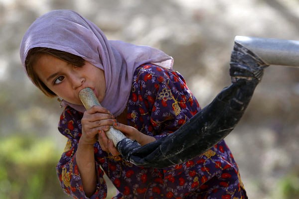 An Afghan girl drinks water from a well through a makeshift faucet in a village in Kandahar Province