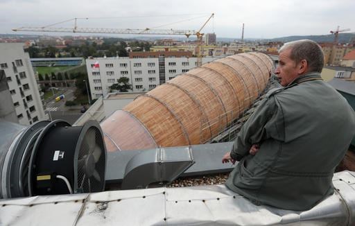 In this Monday, Sept. 19, 2016 photo Leos Valka, a co-creator, sits on a rooftop overlooking a giant object resembling a zeppelin airship at an arts center in Prague, Czech Republic. The 42-meter long and 10-meter wide ship is planned to seat some 120 people on its cascade steps. It will be used for authors' reading and debates about literature to complement exhibitions at the DOX Centre for Contemporary Art, one of the most innovative and challenging galleries in the Czech capital. (AP Photo/Petr David Josek)