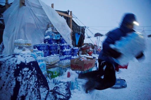 Ray Franks, of New York, trips while carrying a case of water from a storage supply at the Oceti Sakowin camp where people have gathered to protest the Dakota Access oil pipeline in Cannon Ball, N.D., Tuesday, Dec. 6, 2016. Many Dakota Access oil pipeline opponents who've gathered for months in the camp are committed to staying despite wintry weather and demands that they leave. An overnight storm brought several inches of snow, winds gusting to 50 mph and temperatures that felt as cold as 10 degrees below zero. (AP Photo/David Goldman)