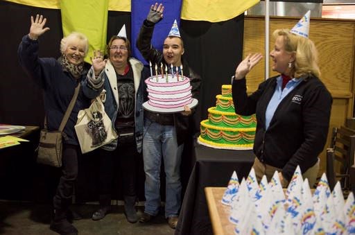 Michele Frymen, from left, Christy Anderson and Jacob Anderson, all from Columbus, hold up a birthday cake and wave as they get their picture taken during some festivities in the food court as part of the 60th birthday celebration for Colo, the nation's oldest living gorilla, at the Columbus Zoo and Aquarium, Thursday, Dec. 22, 2016 in Columbus, Ohio. Colo was the first gorilla in the world born in a zoo and has surpassed the usual life expectancy of captive gorillas by two decades. Her longevity is putting a spotlight on the medical care, nutrition and up-to-date therapeutic techniques that are helping lengthen zoo animals' lives. (AP Photo/Ty Wright)