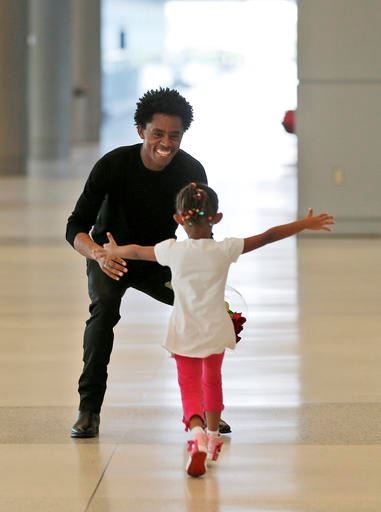 Olympic silver medalist Feyisa Lilesa, left, of Ethiopia, crouches to hug his daughter Soko, 5, while picking up his family at Miami International Airport, Tuesday, Feb. 14, 2017, in Miami. Lilesa arrived in the U.S. on a special skills visa, which allows him to train and compete until January. His wife, son, daughter and brother joined him in Miami Tuesday. (AP Photo/Wilfredo Lee)