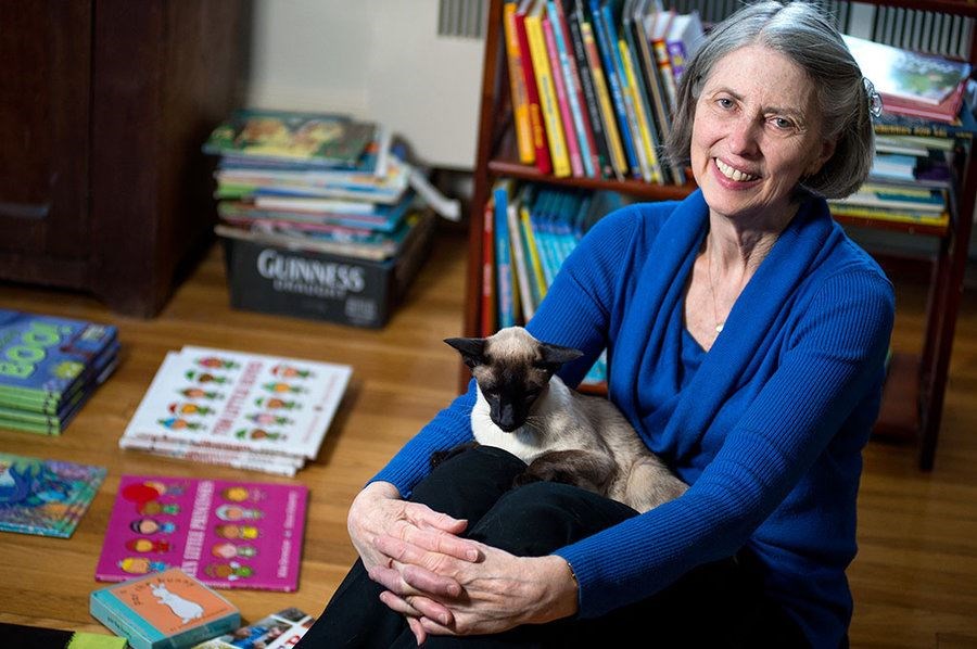 Elizabeth Handel sits with one of her cats in her living room in Needham, Mass., where she sorts donated books. During the holiday giving season, the room can be completely full of books. (Ann Hermes/Christian Science Monitor staff)