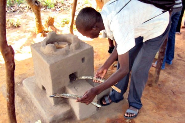 A young man demonstrates how to insert wood into an Esperanza cooking stove in Malawi’s Rumphi North region. The locally produced stoves use less wood, saving forests and easing the lives of families.  <P>Karen Sanje/AlertNet