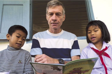 Sasha Alyson (c.) reads ‘New, Improved Buffalo’ – a book he wrote and published in Lao and English – to two children at the elementary school in Pakseuang village in Laos during a ‘book party.’ Mr. Alyson’s group, Big Brother Mouse, aims to ‘make literacy fun for children in Laos.’