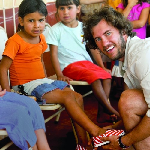 BLake Mycoskie placing shoes on kids in Argentina (http://willfifield.wordpress.com/ ())