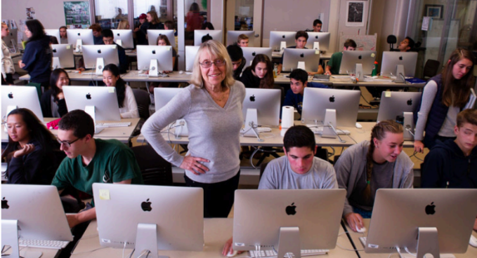 Esther standing in classroom among students and computers