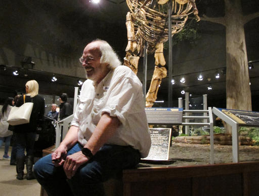 In a Saturday, May 21, 2016 photo, Jack Horner smiles as he sits under Montana's T Rex in the Museum of the Rockies in Bozeman, Mont. The museum hosted