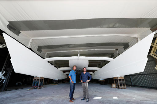 In this photo dated Aug. 31, 2016 and provided by RIVACom, Energy Observer expedition leader Jerome Delafosse, left, and captain, Victorien Erussard, pose in front of the two floats of Energy Observer, which is the first boat to be powered solely by renewable energies and hydrogen, in Saint Malo, western France. The first self-sufficient boat only powered by emission-free energy will start a six-year trip around the world next spring. (Pierrick Contin/Energy Observer via AP)